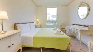 Ein Hotelzimmer mit Bett, Nachttisch, Lampe, Kommode, Schreibtisch und einem Fenster.