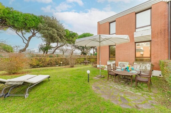 Un patio con mesa y sillas, césped y un edificio de ladrillo.