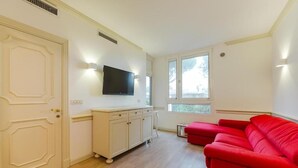 Ein Zimmer mit einem roten Sofa, einem an der Wand befestigten Fernseher, einem Schrank und einer Tür.