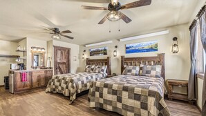 A bedroom with two beds, wooden flooring, ceiling fans, and a vanity with a mirror and lights. - Old West Studio Cabin Near Yellowstone (Island Park)