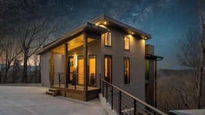 A modern house with a covered porch, large windows, and a starry night sky. - Hot Tub w/ Panoramic Views + Indoor Pool (Sevierville)