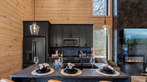 A modern kitchen with dark cabinetry, a central island with seating, and a fireplace. - Hot Tub w/ Panoramic Views + Indoor Pool (Sevierville)