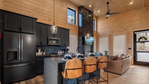 A modern kitchen with dark cabinets, a central island with bar stools, and a dining area with a sofa. - Hot Tub w/ Panoramic Views + Indoor Pool (Sevierville)
