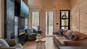 A cozy living room with a fireplace, leather sofas, and a TV mounted on the wall. - Hot Tub w/ Panoramic Views + Indoor Pool (Sevierville)