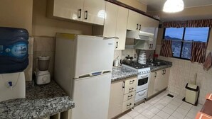 Una cocina con armarios blancos, un refrigerador, una estufa y una ventana con cortinas.