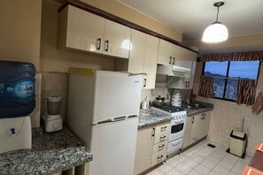 A kitchen with white cabinets, a refrigerator, a stove, and a window with curtains. - Apartment with a breathtaking view of the Illimani, (La Paz)