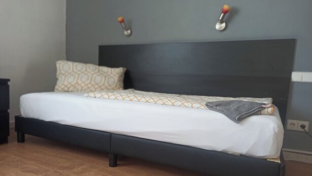 A bed with a dark headboard, a white mattress, and a patterned pillow. - Accommodation for up to 25 people / from 15-per person (Waldbronn)