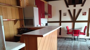 A kitchen with wooden cabinets, a white countertop, and a tiled floor. There is a small dining area with a table and two red chairs. - Accommodation for up to 25 people / from 15-per person (Waldbronn)