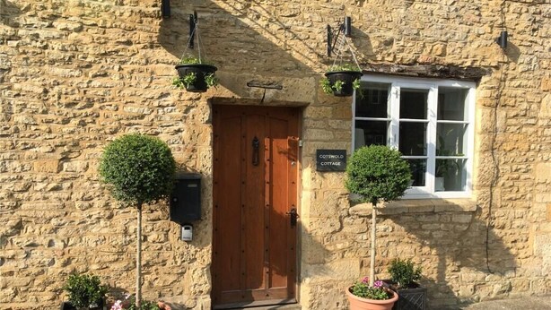 A stone cottage with a wooden door, a window, and hanging plants.