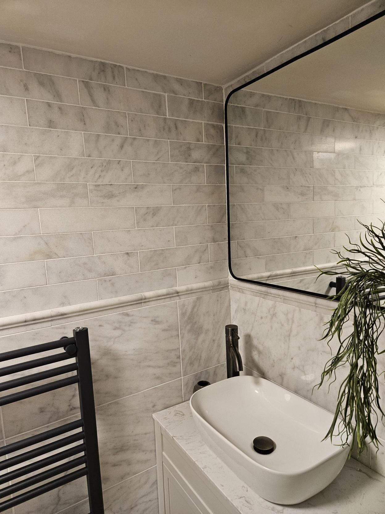A bathroom with a white sink, a black towel rack, and a mirror on the wall.