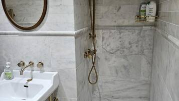 A bathroom with a white sink, a mirror, a shower with a handheld showerhead, and a shelf with toiletries.