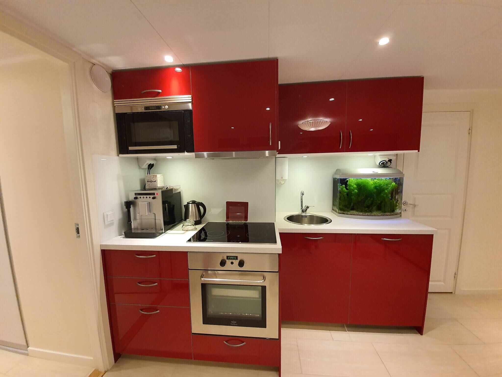 Una cocina compacta con gabinetes rojos, un microondas, una cafetera, un horno y un acuario.