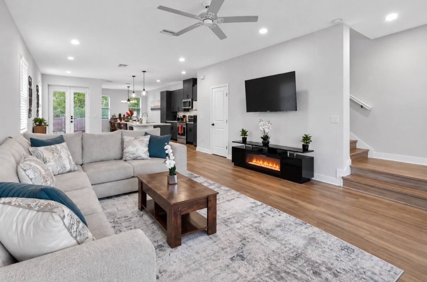 A modern living room with a sectional sofa, a coffee table, a fireplace, and a TV mounted on the wall.