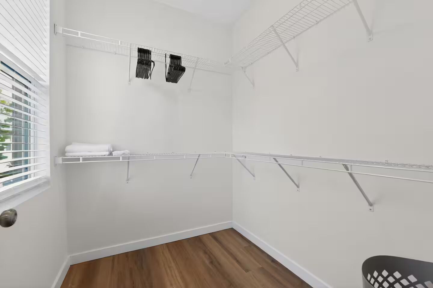 A closet with metal shelves, a wooden floor, and a window with blinds.