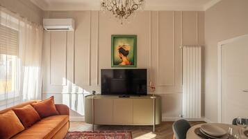 Un soggiorno con un divano, una TV su un mobile, un lampadario e un quadro appeso al muro.