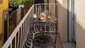 Un balcón con mesa y sillas, un pequeño jardín y vistas de edificios cercanos.