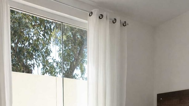 Quarto com cama, porta de vidro deslizante para uma varanda e vista para árvores.
