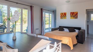 Quarto de hotel com cama, mesa de jantar com cadeiras, um vaso de flores e vista para o exterior.