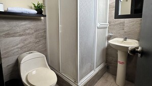 Un baño moderno con inodoro, lavamanos pedestal y cabina de ducha.