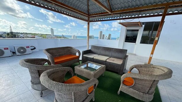 Un espacio de estar techado al aire libre con mobiliario de mimbre y vistas a la ciudad.