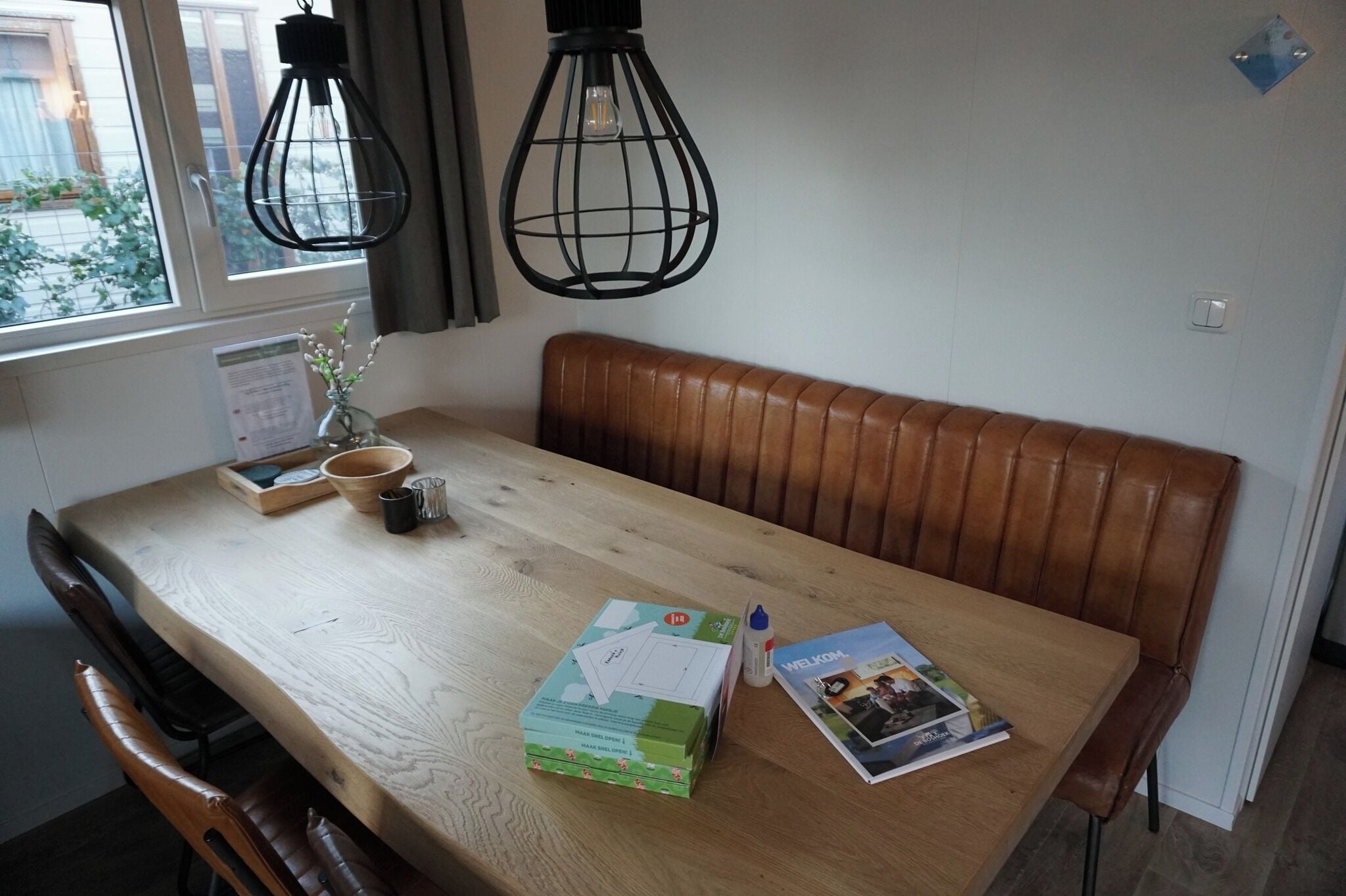 A wooden dining table with a bench, a vase with flowers, a box of tissues, and a magazine.
