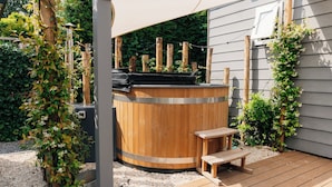 Ein hölzernes Whirlpool mit Sitzbank, umgeben von Grünpflanzen und einer Holzterrasse.