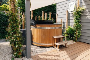 Ein hölzernes Whirlpool mit Sitzbank, umgeben von Grünpflanzen und einer Holzterrasse.