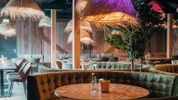 Ein Restaurant mit runden Tischen und gepolsterten Sitzgelegenheiten, ausgestattet mit Strohdächern und Zimmerpflanzen.