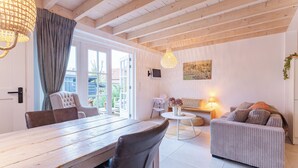 A spacious living room with a wooden dining table, a sofa, and a TV mounted on the wall. - Holiday home - Schoolstraat 6a | Vrouwenpolder (Vrouwenpolder)