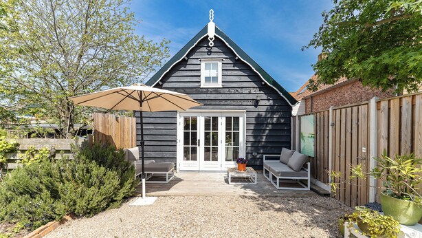 A wooden house with a gravel patio, a white door, and a small garden with potted plants. - Holiday home - Schoolstraat 6a | Vrouwenpolder (Vrouwenpolder)