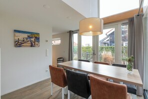 A dining area with a wooden table and chairs, a hanging light fixture, and a painting of a beach scene on the wall. - Zonnedorp 21  Beach Villa Joya Renesse | Luxury Beach Villa with Sauna (Renesse)