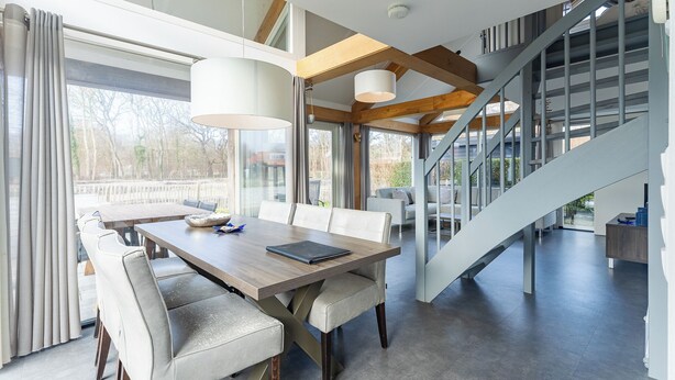 Een modern interieur met een eethoek, een trap en grote ramen.