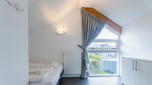Een slaapkamer met een bed, een radiator, een raam met gordijnen en uitzicht op buiten.