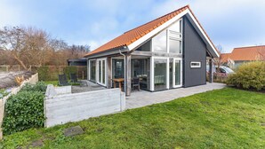 Een modern huis met een schuin dak, grote glasramen en een overdekt terras.