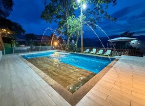 A swimming pool with a wooden deck and lounge chairs, surrounded by trees and night lighting. - Ecohotel Alflo (Villeta)