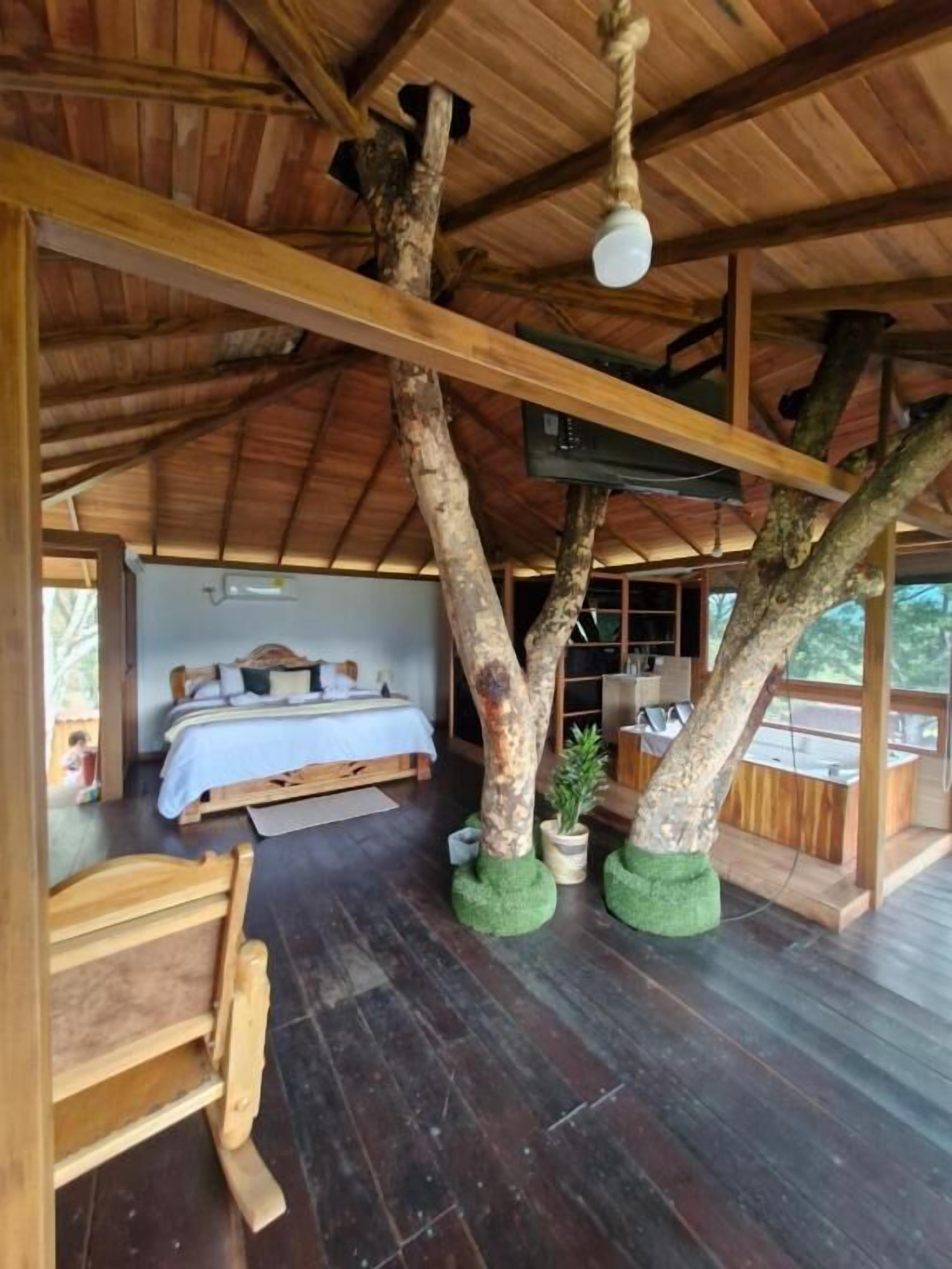 A rustic wooden room with a bed, a dining table, and a staircase.