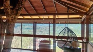 A wooden interior with a view of the outdoors, a wooden chair, and a table with a hanging chair outside.