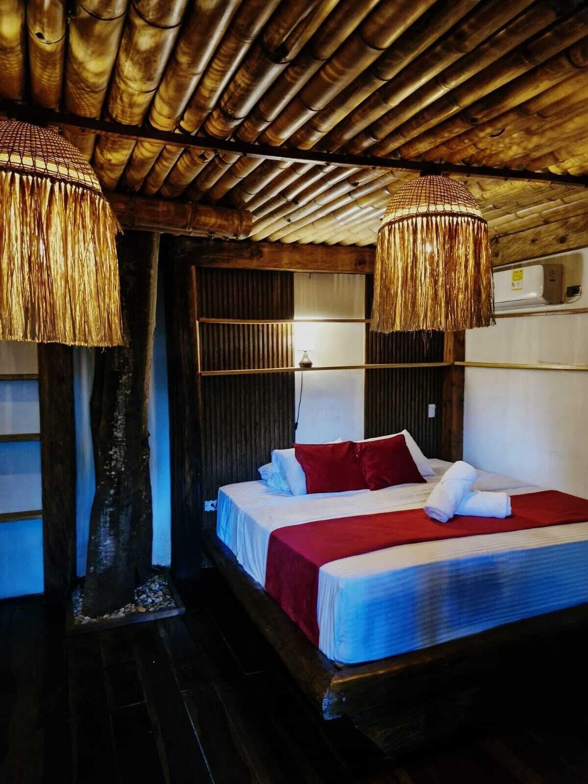 A room with a bed, a wooden ceiling, and two hanging lamps.
