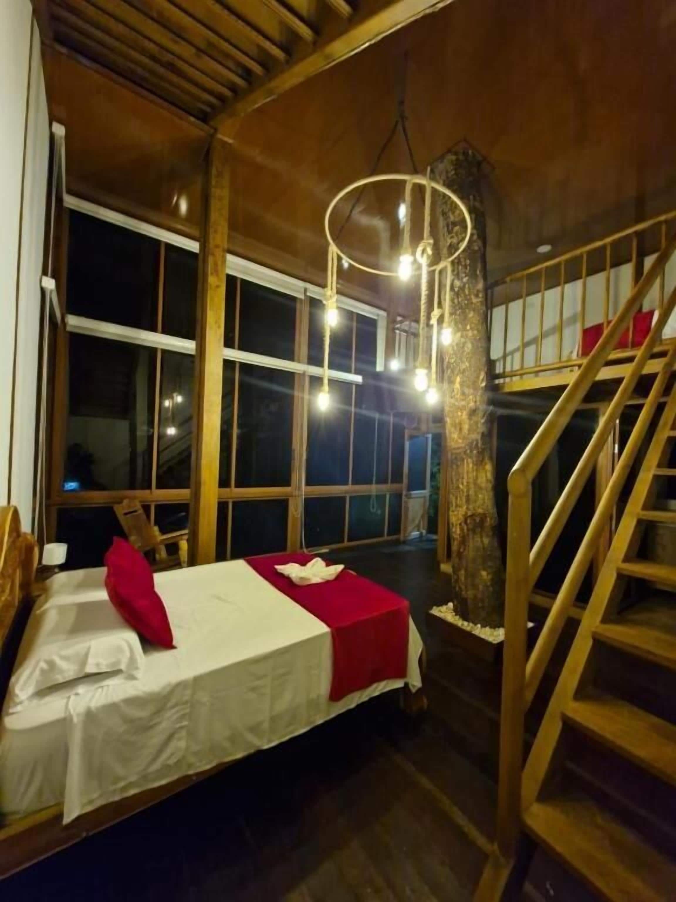 Une pièce avec un lit, un escalier en bois et de grandes fenêtres.