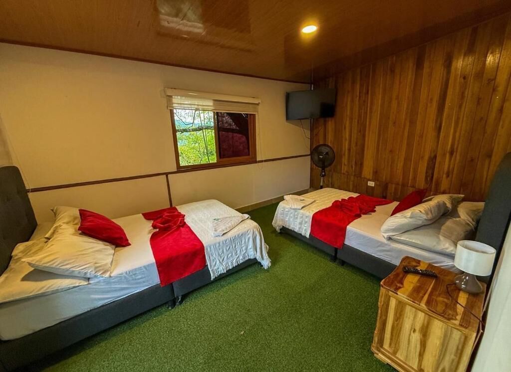 A room with two beds, a window, a fan, and a wooden nightstand.