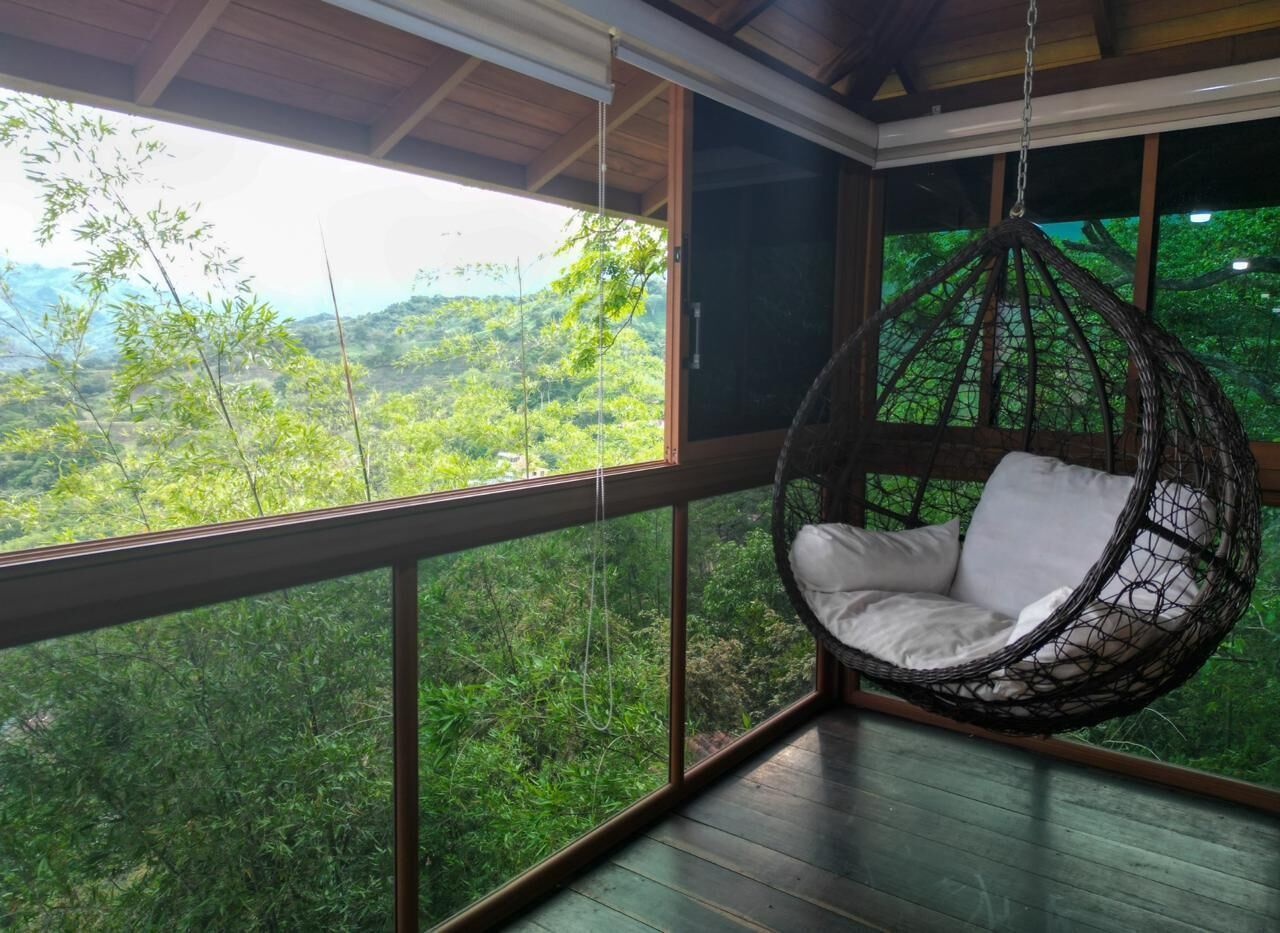 Una silla colgante en una habitación con ventanas amplias que dan a un paisaje verde exuberante.
