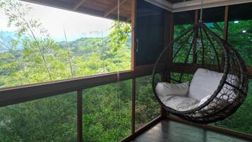 Una silla colgante en una habitación con ventanas amplias que dan a un paisaje verde exuberante.