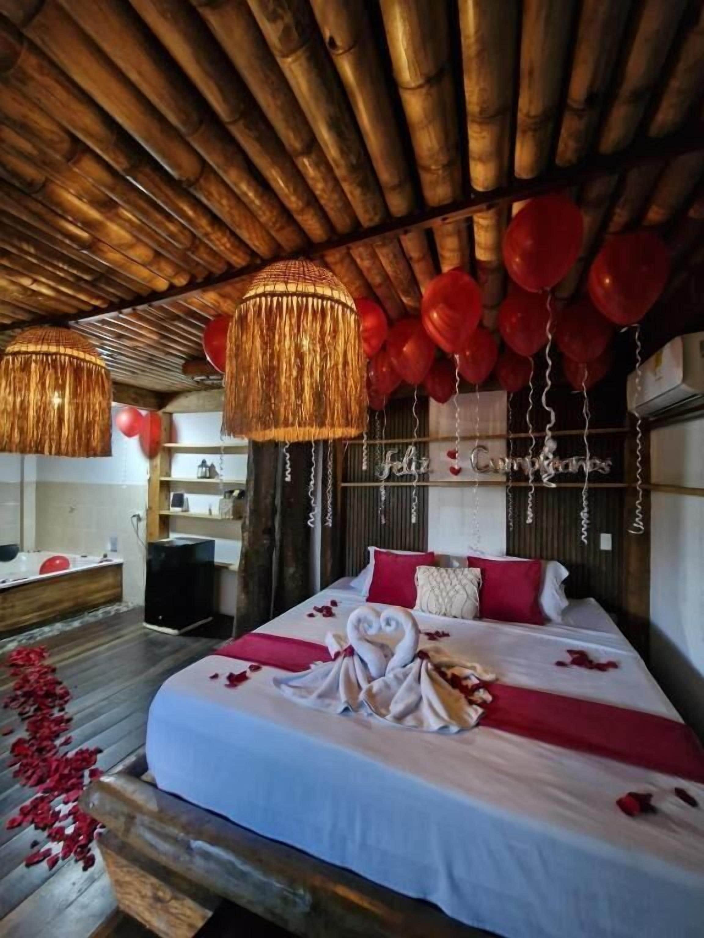 A bedroom with a wooden ceiling, a bed with red and white bedding, and a string of red balloons.