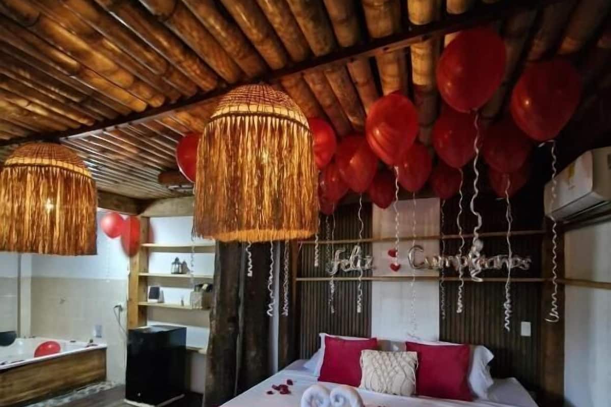 A bedroom with a wooden ceiling, a bed with red and white bedding, and a string of red balloons.