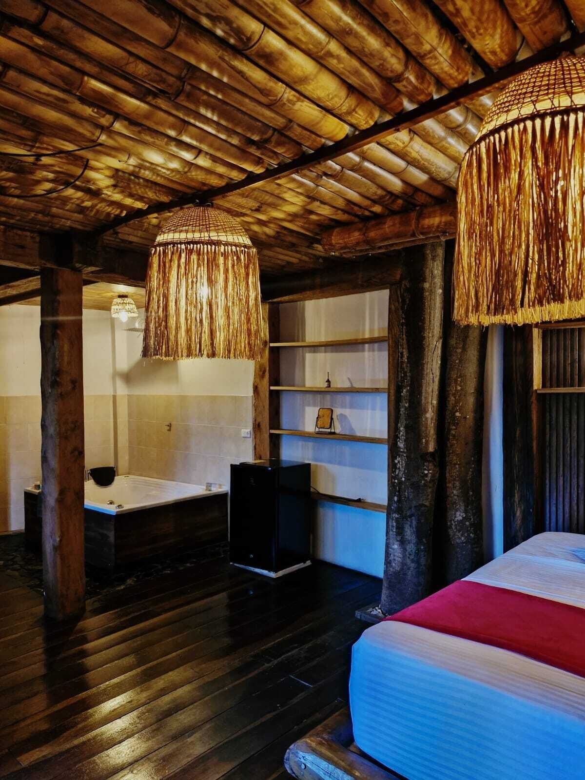 A rustic room with a wooden ceiling, a large bed, a bathtub, and a wooden shelf.