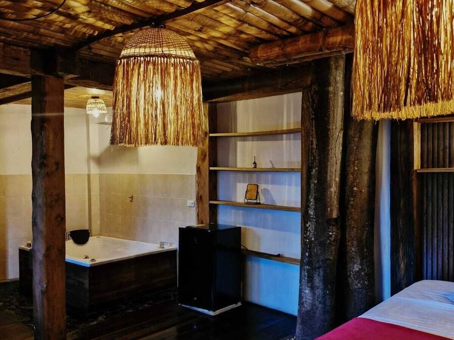 Una habitación rústica con techo de madera, una cama grande, una bañera y un estante de madera.