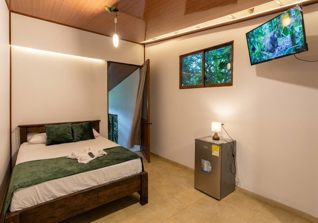 A bedroom with a bed, a television, a small cabinet, and a door leading to another room.