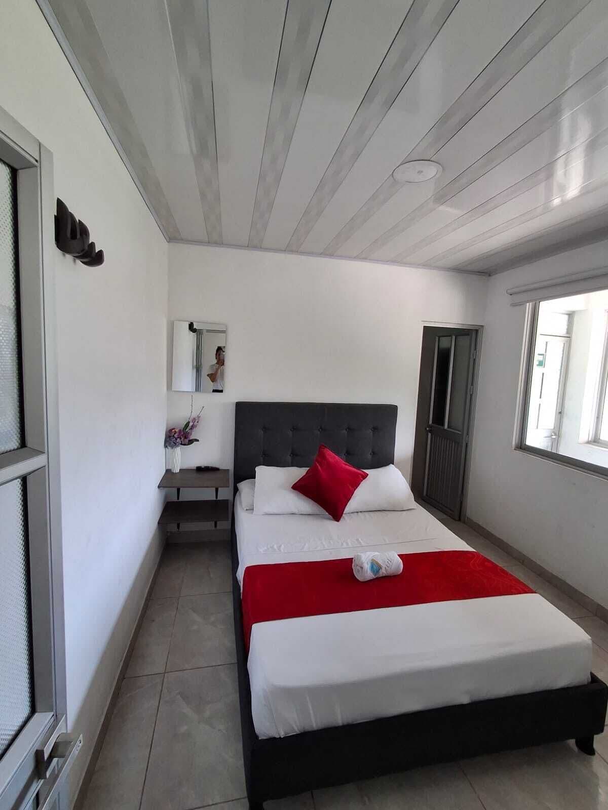 A bedroom with a bed, a bedside table, a mirror, and a window.