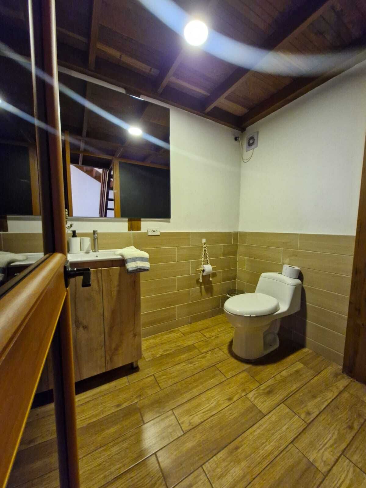 Un baño con suelo de madera, inodoro, lavabo con espejo y un perchero para toallas.