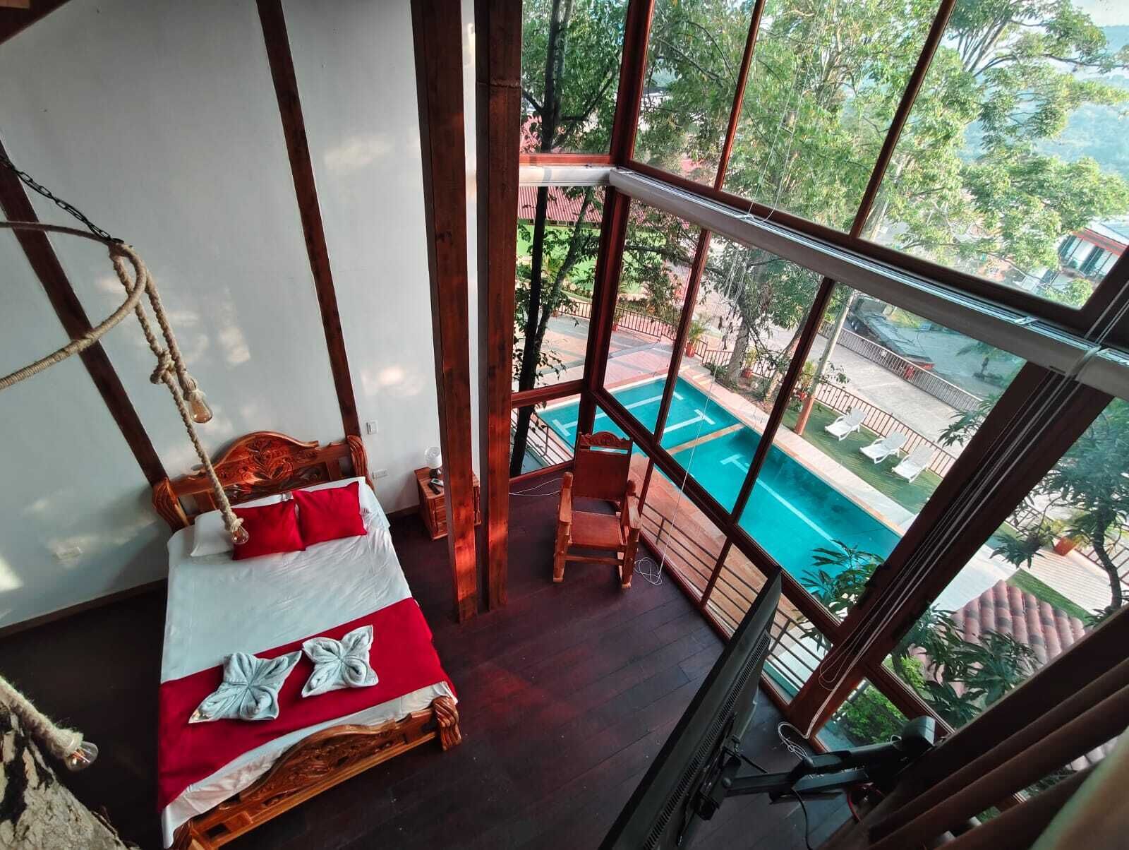 A bedroom with a wooden bed, a small table, and a view of an outdoor swimming pool.